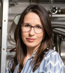 Frau Reichlova mit Brille und langen Haaren vor technischem Hintergrund.